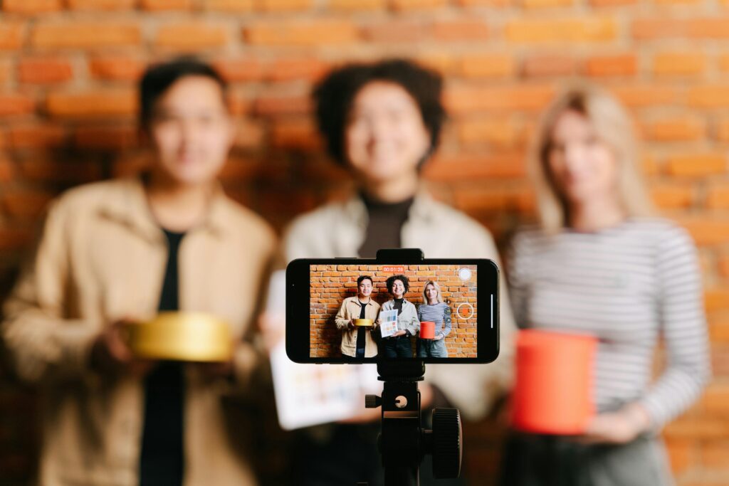 A diverse team of vloggers recording a video with a smartphone against a brick wall backdrop.